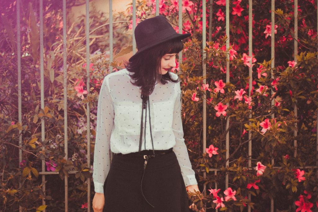 the Urban herbalist stands in front of a gate and looks at wild pink flowers